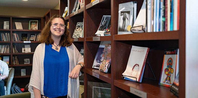 Emily Hizny stands in front of a bookcase.